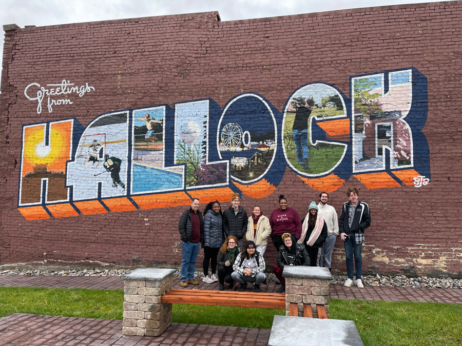 Student group poses in front of a wall with a City of Hallock mural