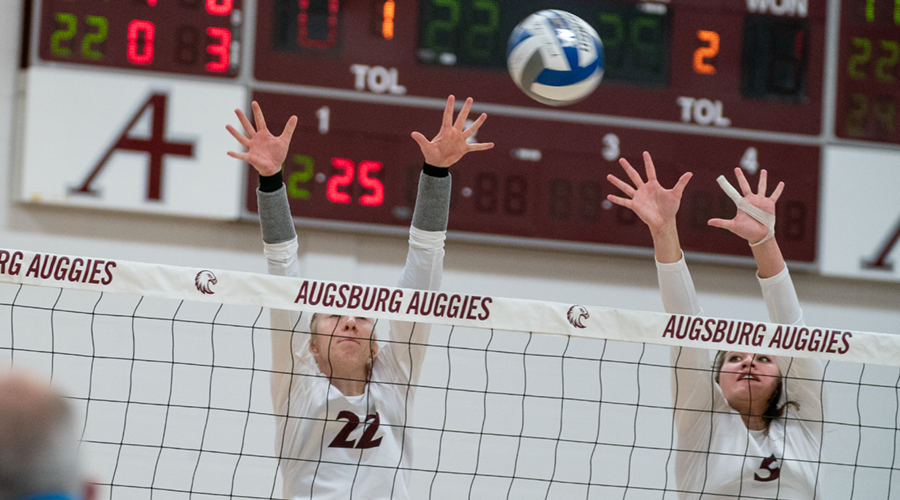 Augsburg volleyball players block the ball against St. Olaf College, 2021. (Photo by Courtney Perry)