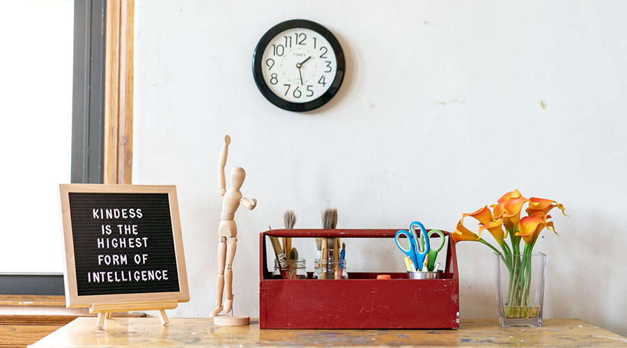 Workspace with letter board, wooden figure, red toolbox with tools, orange flowers, and a clock on the wall.
