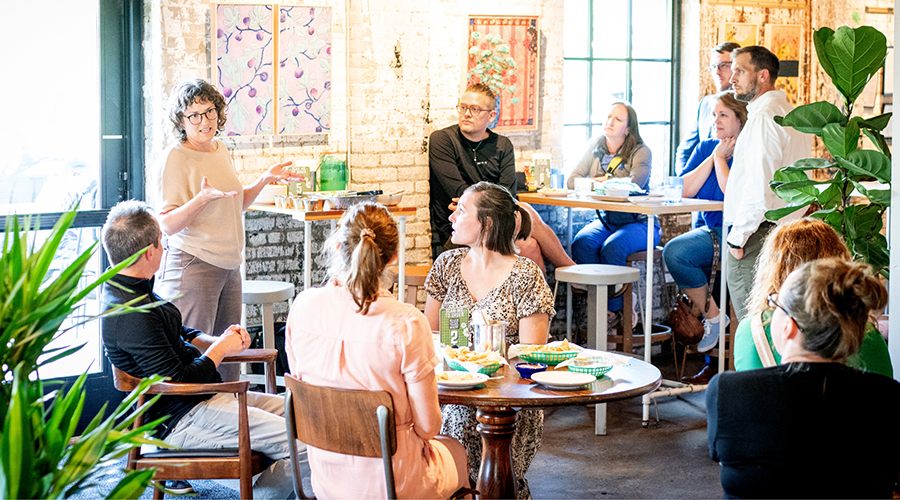Casual group meeting in a café-style space with a woman speaking to seated attendees.