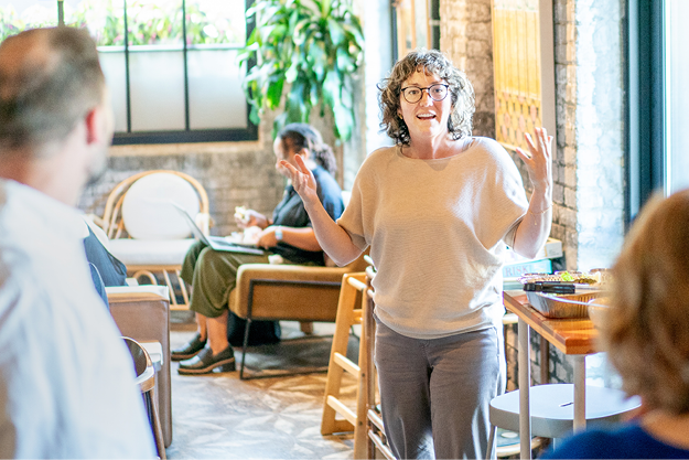 Person speaking in a bright, casual office setting with furniture and plants.