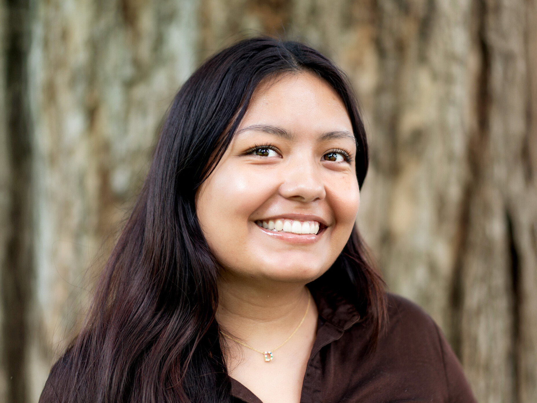 Diana Reyes headshot: she has long dark hair and is smiling, standing in front of a tree
