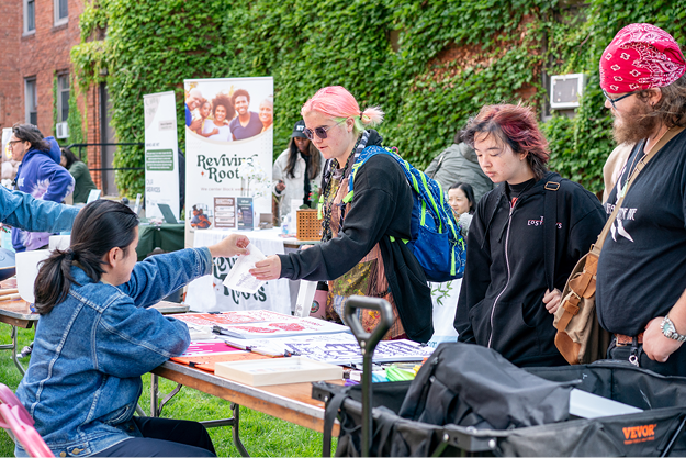 People interacting at an outdoor event with tables and informational materials.