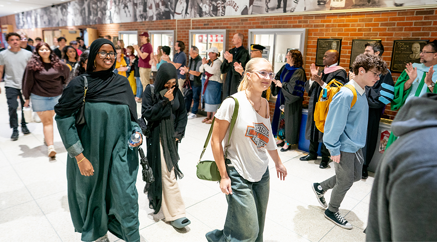 A group of people walking through a hallway lined with clapping individuals, some in academic gowns.