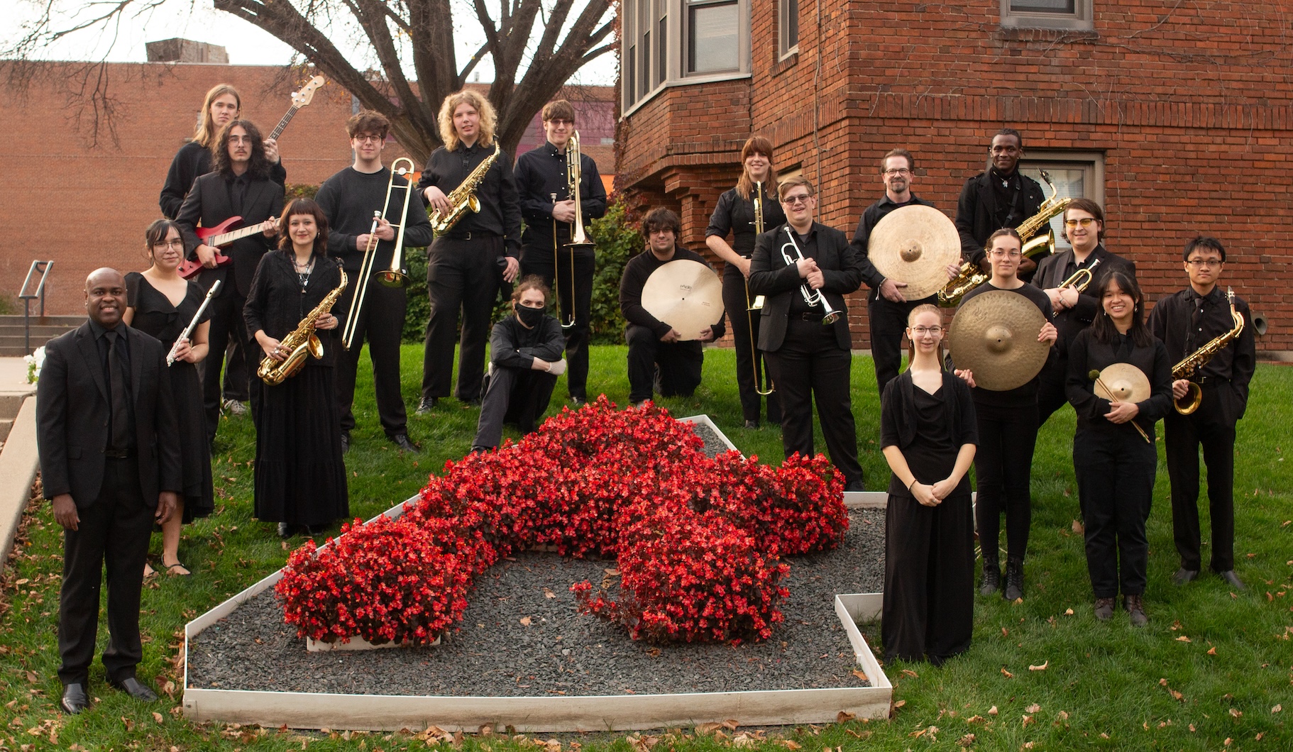 Dressed all in black and holding their instruments, members of the Augsburg Jazz Ensemble surround the floral "A" outside of Memorial Hall.