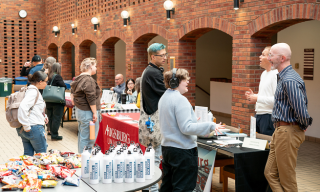 People gathered around tables with snacks and informational materials under brick archways, featuring an Augsburg University table.