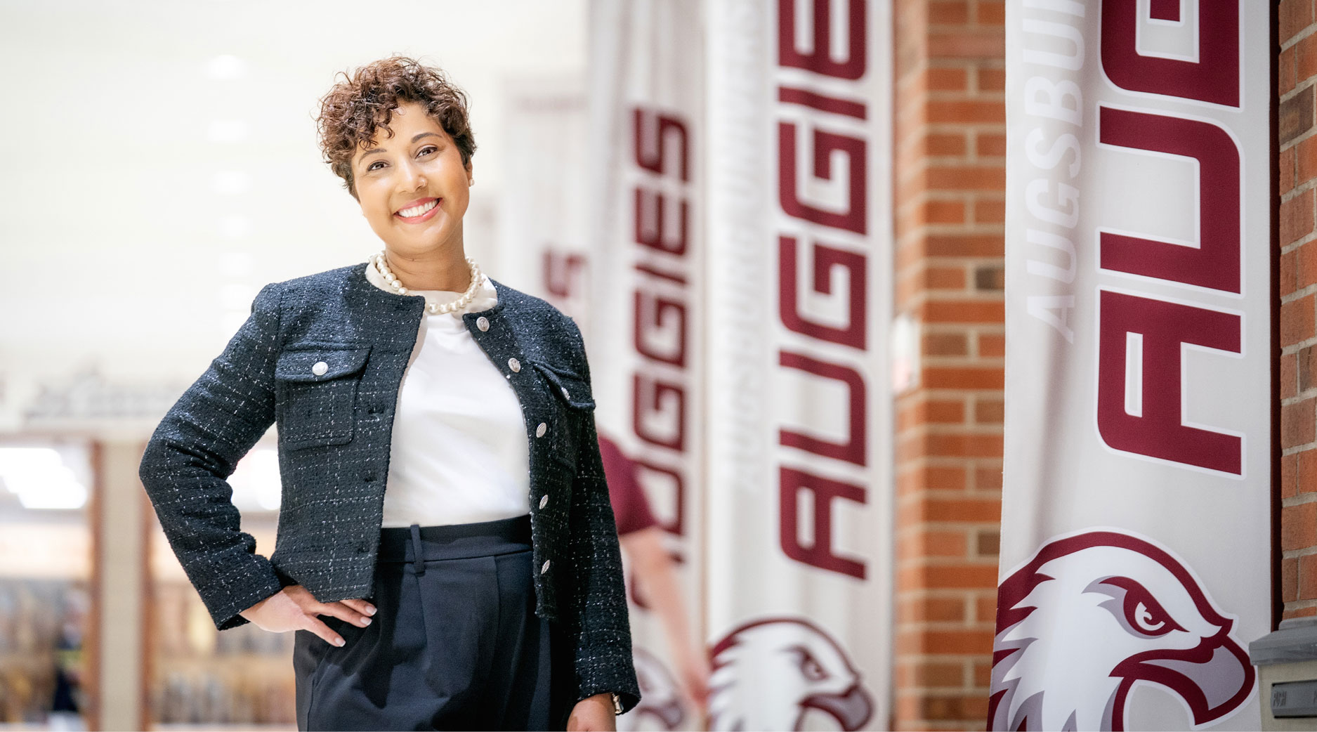 A person stands confidently beside banners with "Auggies" written on them and an eagle emblem.