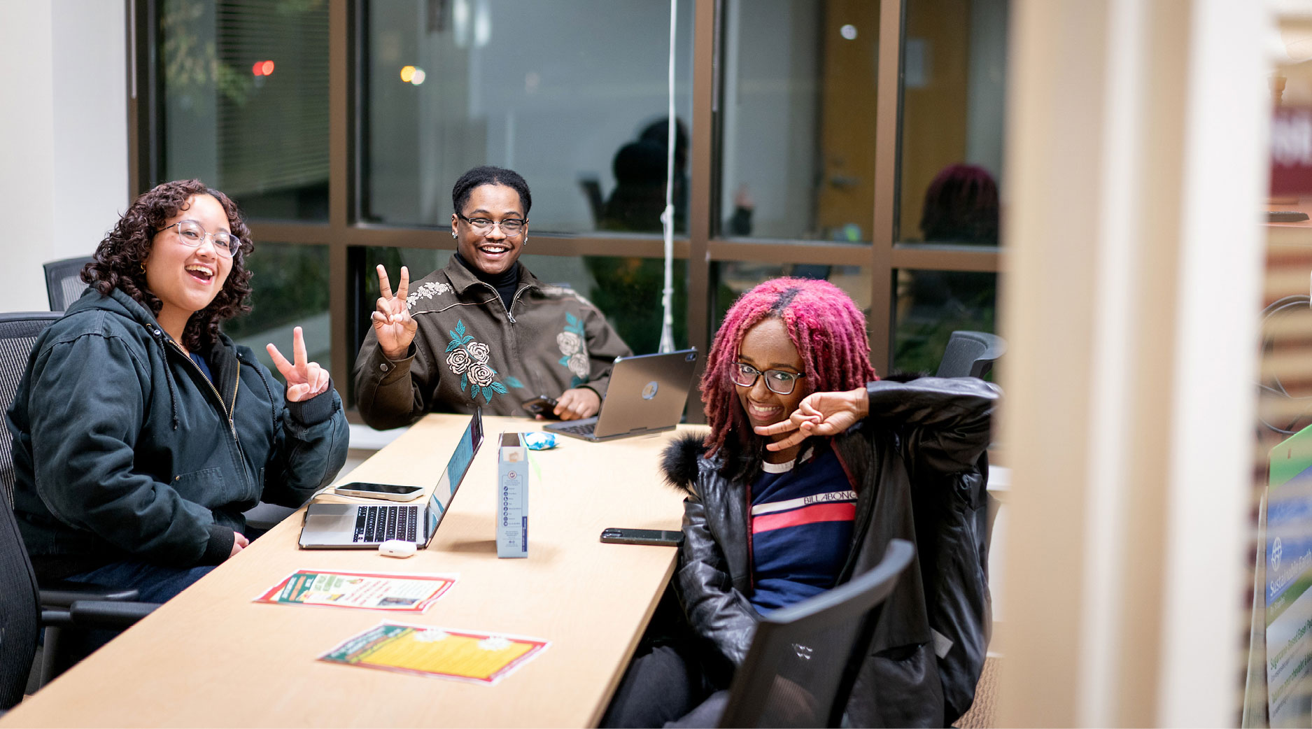 Header-Bonner-Leaders Three people sitting at a table with laptops, smiling and making peace signs.