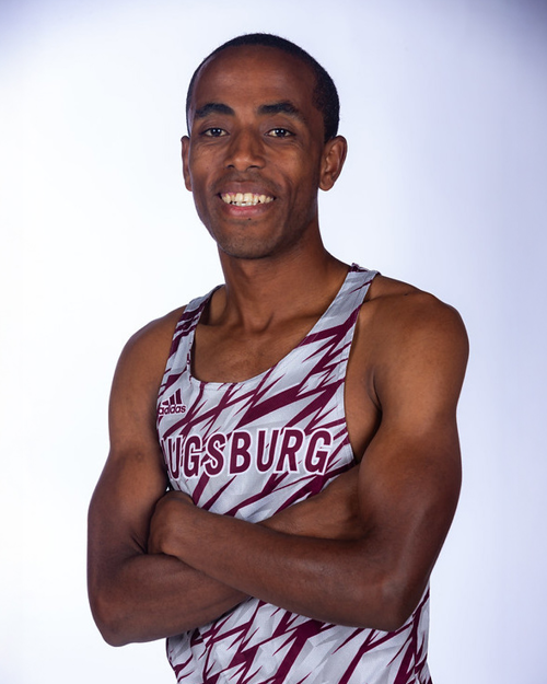 Headshot of Mohammed Bati, a smiling young Black male athlete, wearing a maroon and white Augsburg University athletic tank top with his arms crossed.