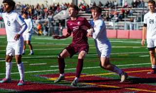 Two soccer players, one in maroon, one in white, grappling for the ball.