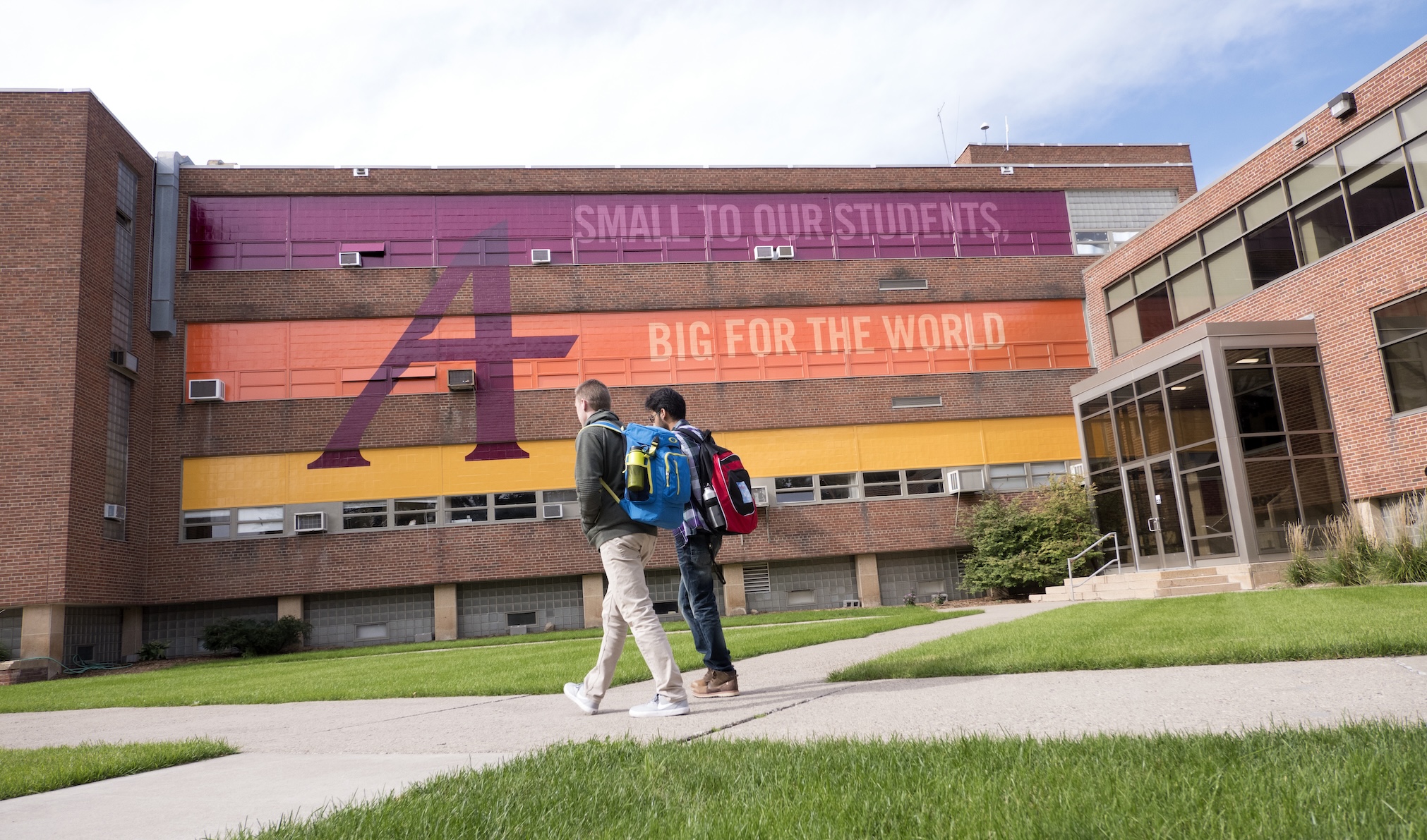 Two Augsburg students walk across the quad in front of the mural on the Old Science Building.