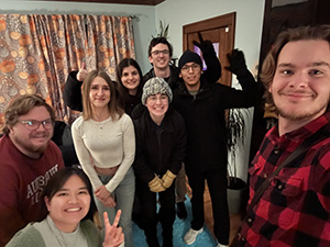 A group of eight diverse young adults smiling for a selfie in a cozy living room.