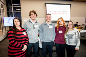A group of five smiling students posing in front of a screen that says "Welcome to the 3rd Annual Auggie Entrepreneur Cup."
