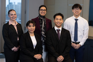 Five students in professional business attire posing for a group portrait in an office setting.