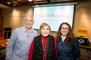 Three faculty members smiling in front of a projection screen that reads "School of Business, Business and Economics."