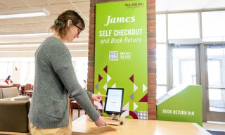 A woman using a digital tablet at a bright green self-checkout and book return station inside the library.