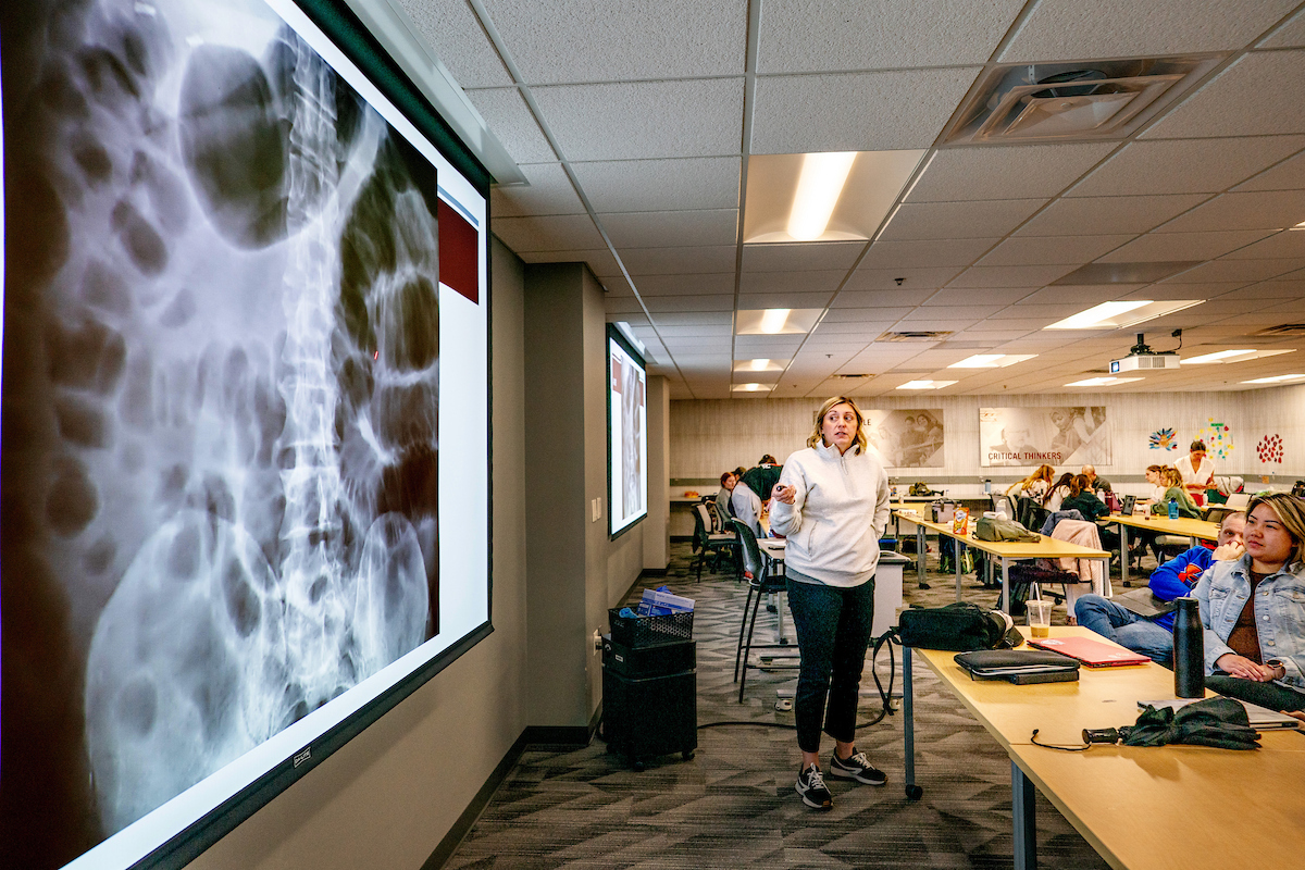 A PA faculty member discusses a large X-ray illuminated on a screen in front of a classroom of students.