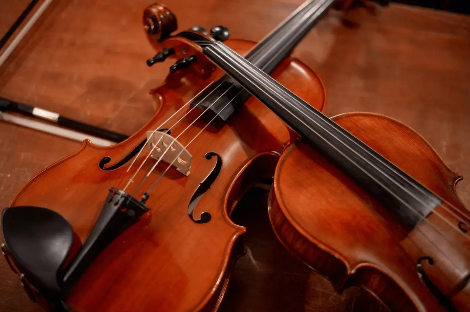 Two restored Holocaust-era violins resting with their necks crossed against a wooden background.