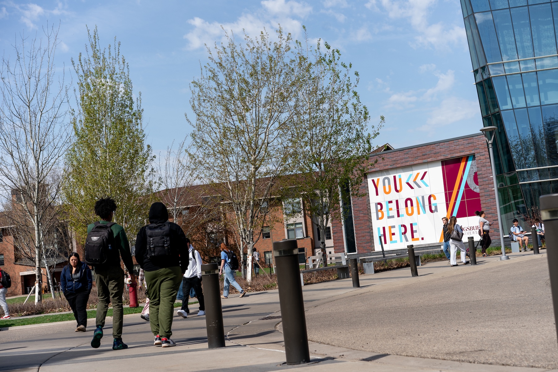 Students on campus walk in front of the Hagfors Wall reading, You Belong Here