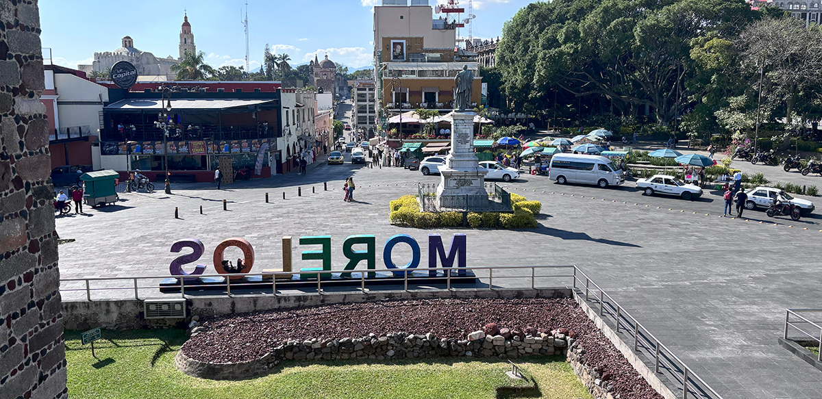 00__Feature Image Elevated view of a sunny city plaza in Morelos featuring large, colorful "MORELOS" letters, a central monument, and surrounding buildings.