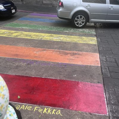 IMG_5637 High-angle view of a street crosswalk painted in rainbow pride colors with a silver car parked near it.