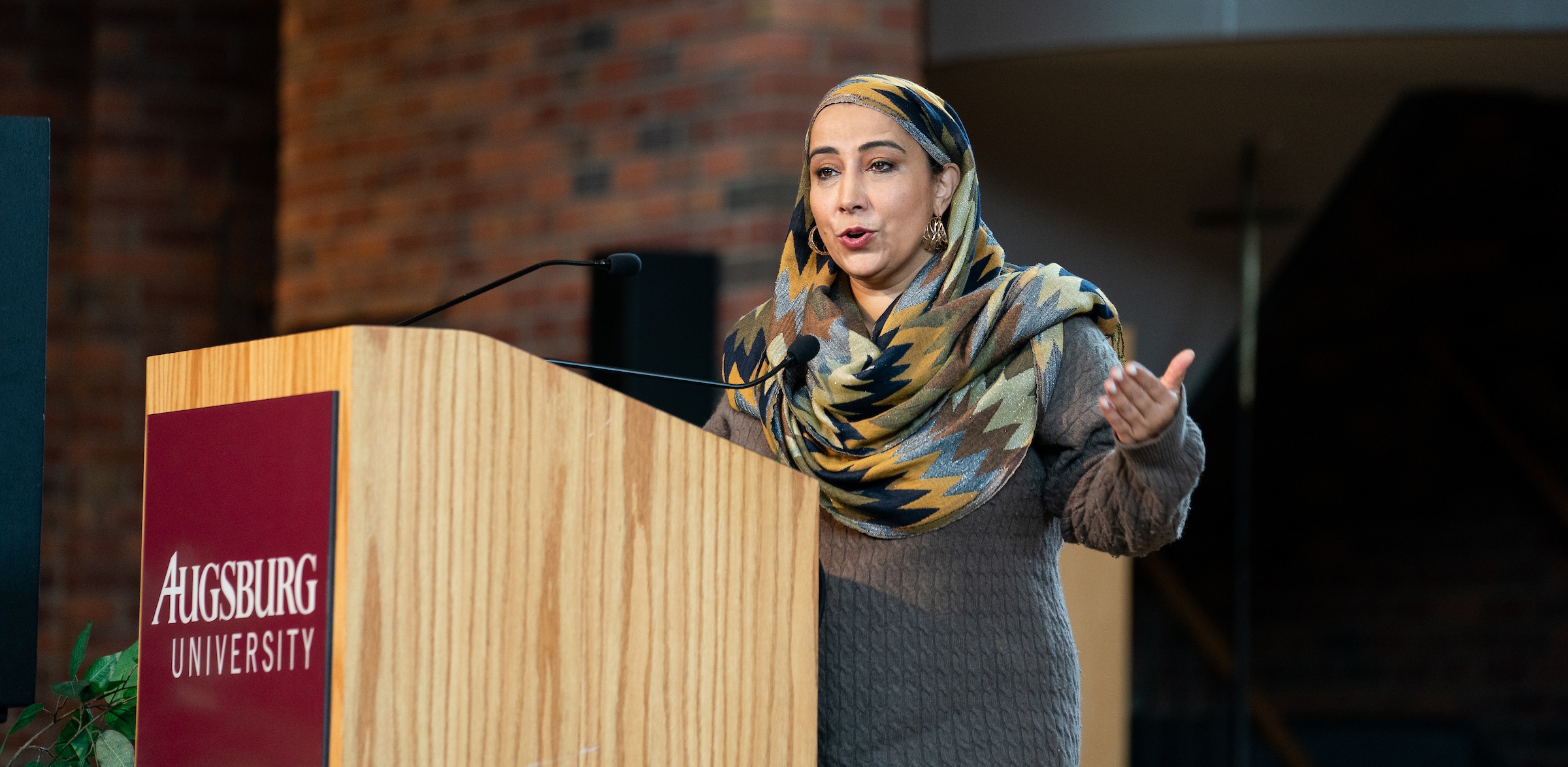Najeeba Syeed wears a gray sweater and a zig-zag patterned headscarf while speaking at a lectern in Hoversten Chapel.