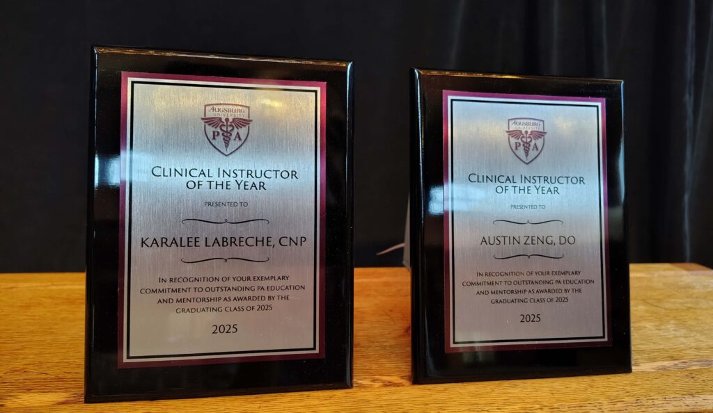 two shiny black and silver plaques with the title 'clinical instructor of the year' celebrating karalee labreche and austin zeng. They are on a wooden table with a black background.
