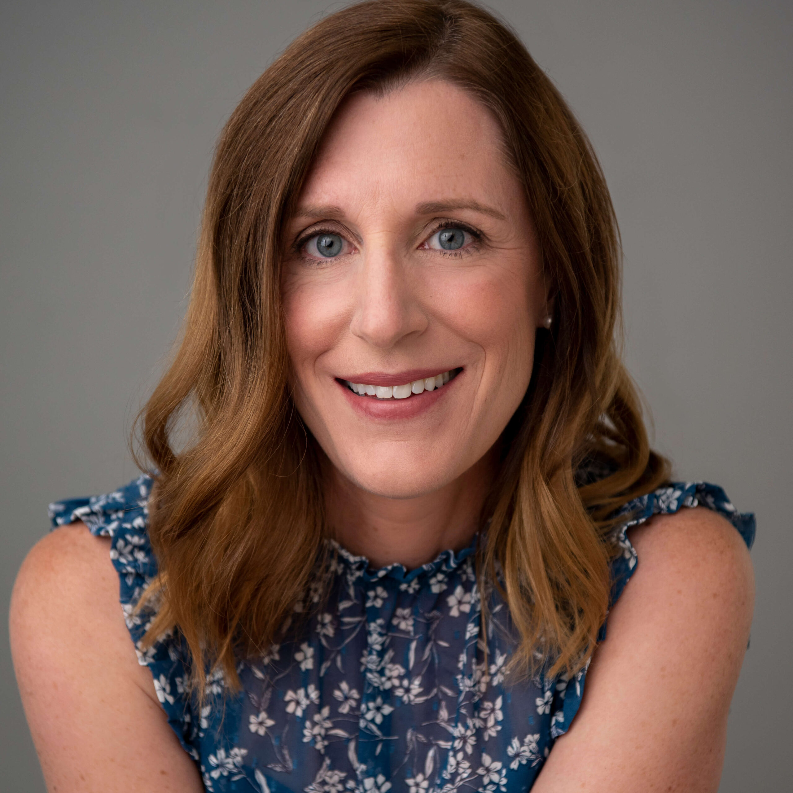 Headshot of Michelle smiling at the camera. She is in a dark blue shirt with a floral pattern. Her brown hair is down and wavy to her shoulders.
