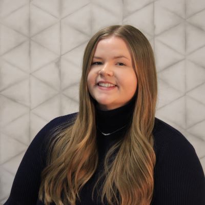 headshot of Alexis, a white woman, wearing a black turtleneck shirt and smiling at the camera. Her blond hair is past her shoulders and in front of her shirt.