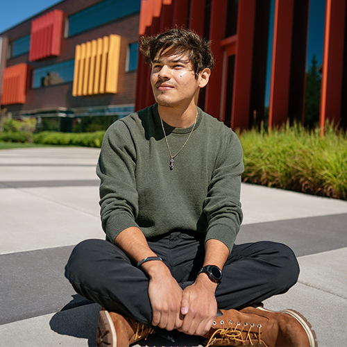 Young person sitting on the ground cross-legged.