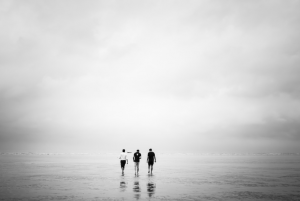 three people walking on cloudy beach 