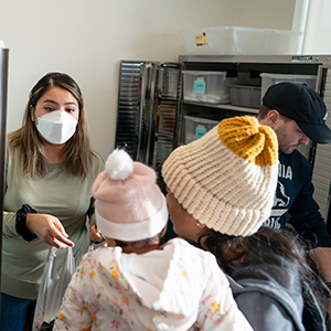 An Augsburg student handing a bag to a woman and her child.