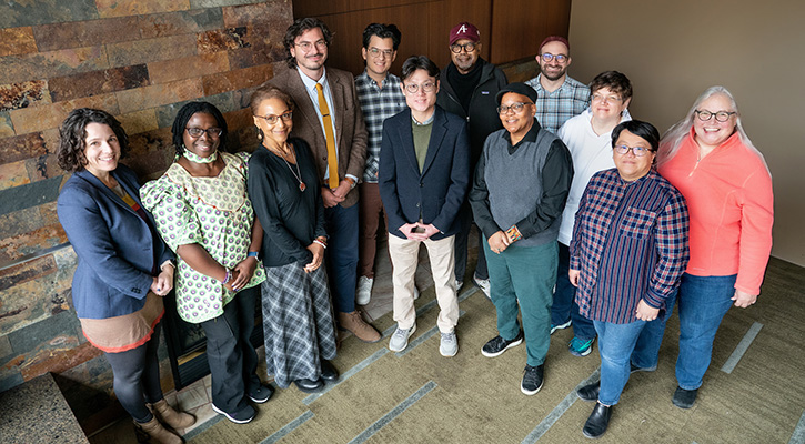 A group of twelve diverse individuals posing in front of a stone wall in a formal setting.