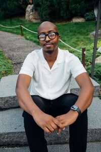 Zakariya Abdullahi posing for a picture on a concrete step with his hands folded and resting on his knees.