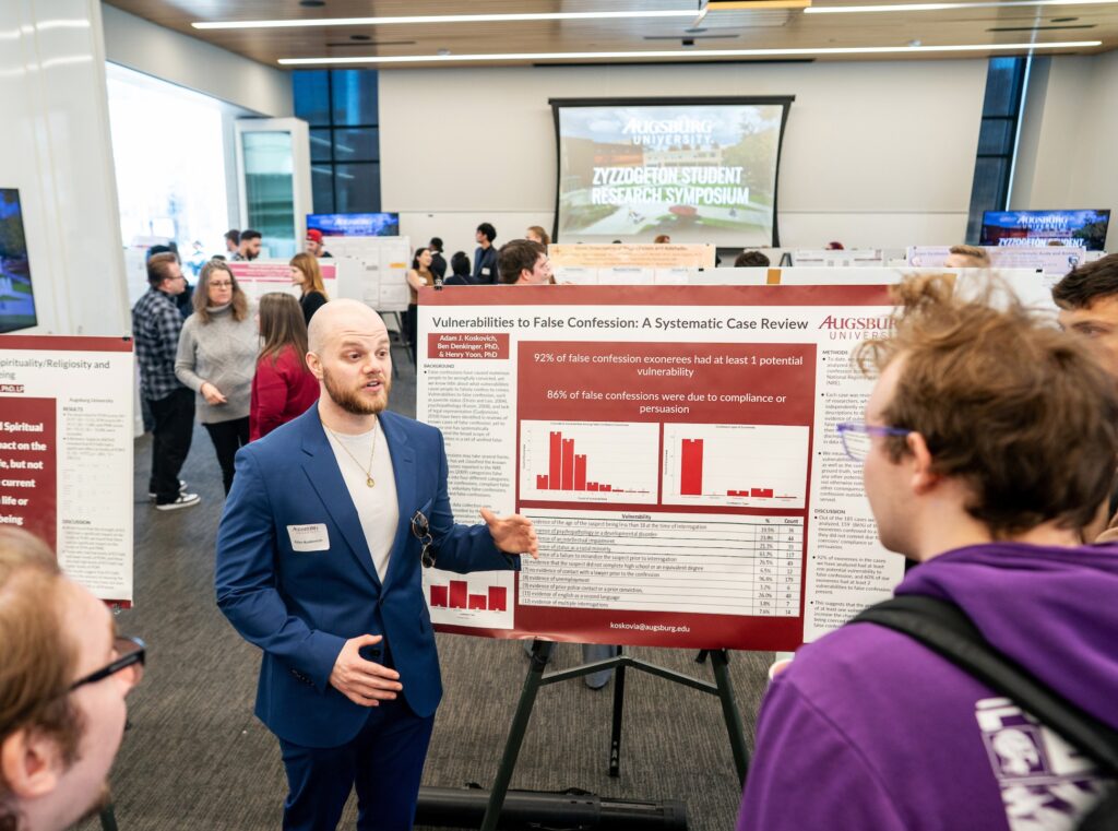 Student in front of research poster presenting to another student.