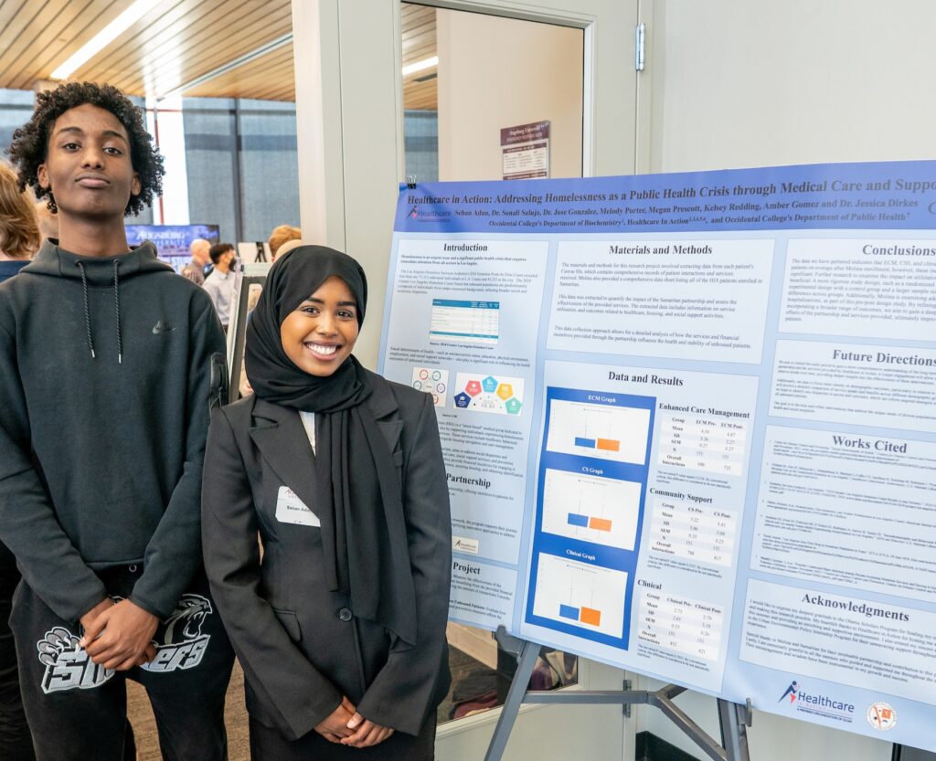 Two students standing ear research poster board.